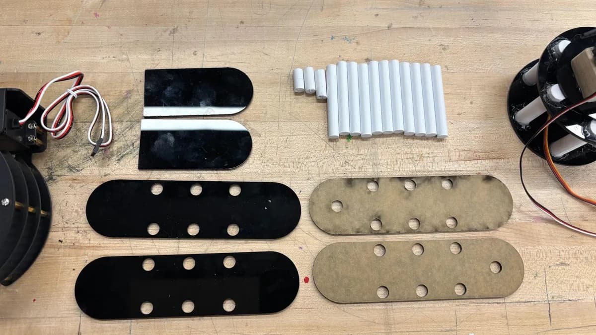 Laser-cut arm links in black acrylic and light wood laid out on a bench with standoffs and a servo.