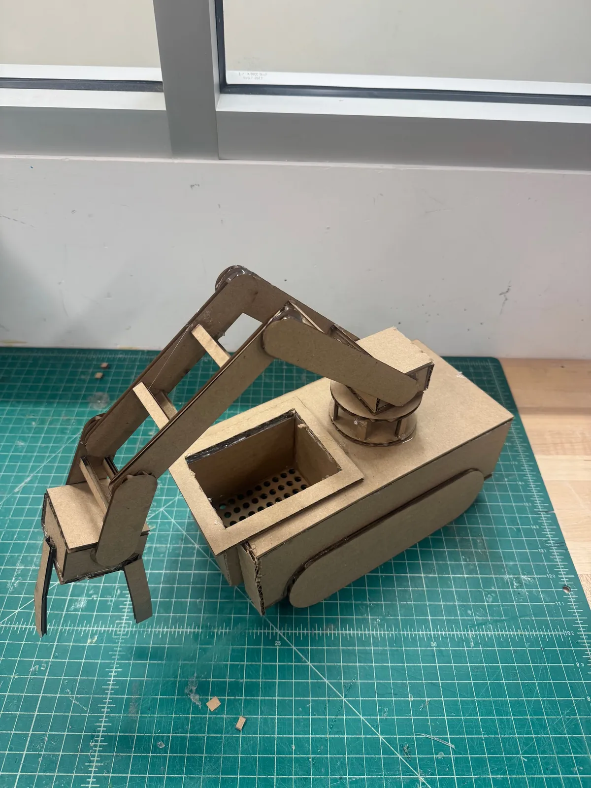 An early cardboard mock-up of the robot with a perforated sifter bin and a jointed cardboard arm.