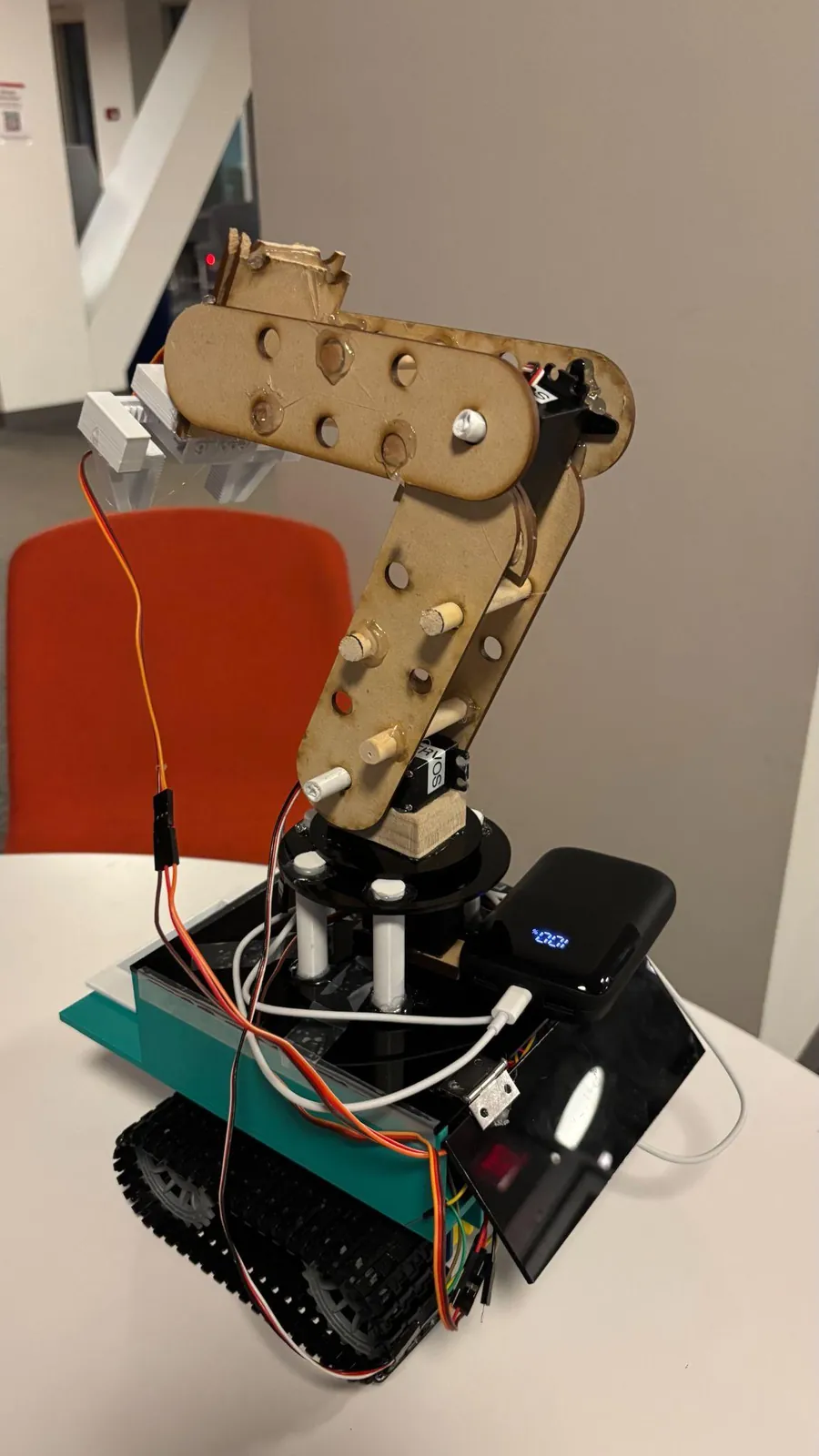 The final build: a laser-cut low-density wood arm with servos at the joints and a 3D-printed claw, on the tracked teal chassis.