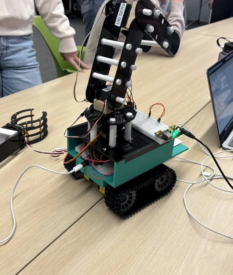 ShoreClear on a classroom table: a teal body on black tank tracks with a black laser-cut acrylic arm and a breadboard on top.